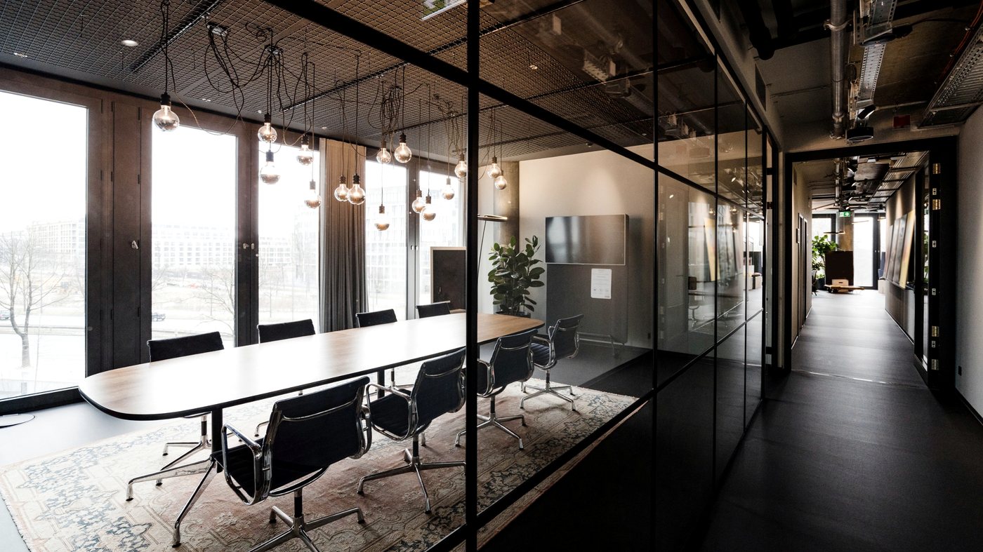 A glass walled meeting room with a long timber table and pendant lights